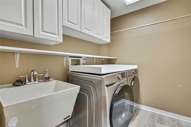 washroom with cabinet space, baseboards, light wood-type flooring, separate washer and dryer, and a sink