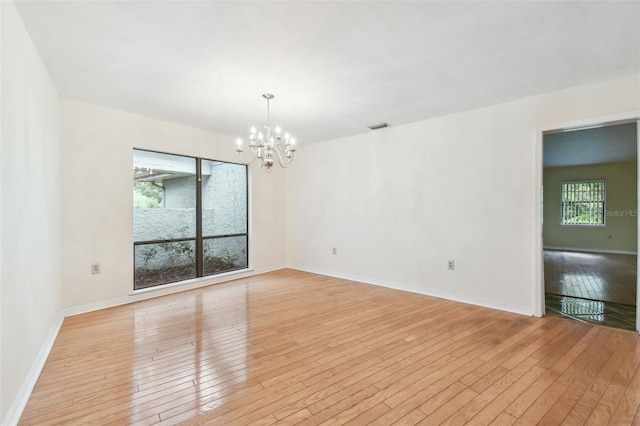 spare room with light wood-style floors, visible vents, baseboards, and an inviting chandelier