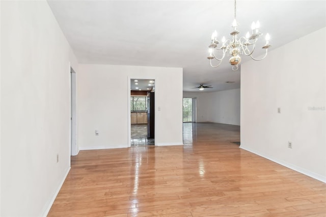 spare room featuring ceiling fan with notable chandelier, light wood-style flooring, and baseboards