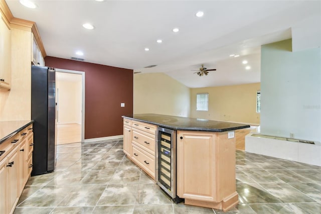 kitchen with light brown cabinets, beverage cooler, freestanding refrigerator, a center island, and dark stone countertops