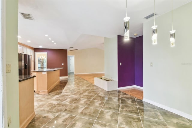 kitchen with visible vents, open floor plan, dark countertops, stainless steel fridge, and pendant lighting