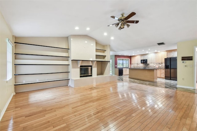 unfurnished living room with a large fireplace, baseboards, lofted ceiling, ceiling fan, and light wood-type flooring