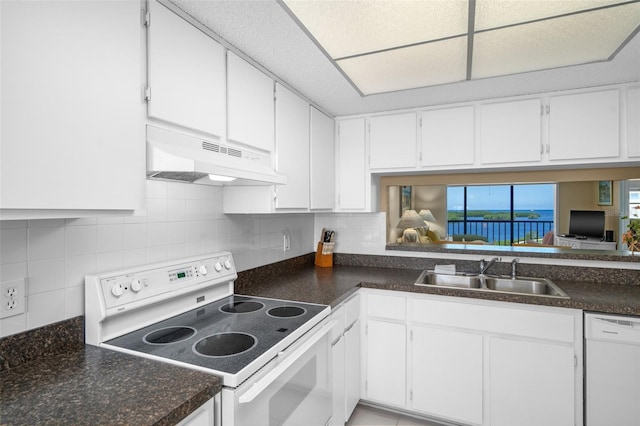 kitchen featuring dark countertops, white cabinets, a sink, white appliances, and under cabinet range hood