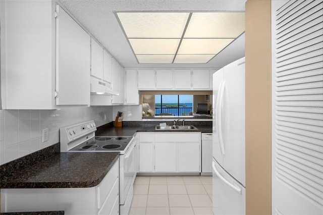 kitchen featuring dark countertops, white appliances, under cabinet range hood, and white cabinets