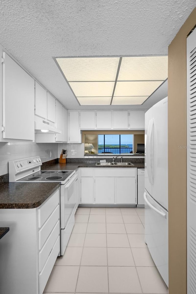 kitchen with white appliances, under cabinet range hood, white cabinetry, a sink, and light tile patterned flooring