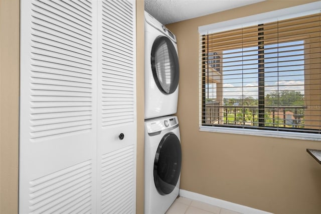 laundry area with stacked washer and clothes dryer, light tile patterned floors, a textured ceiling, laundry area, and baseboards