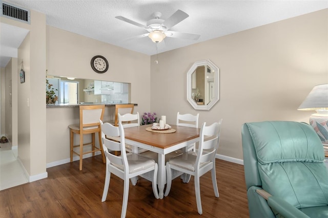 dining space featuring a textured ceiling, visible vents, baseboards, a ceiling fan, and dark wood finished floors