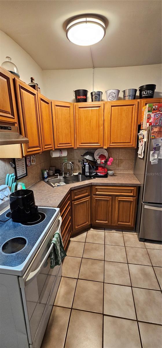 kitchen with electric stove, light countertops, freestanding refrigerator, a sink, and under cabinet range hood