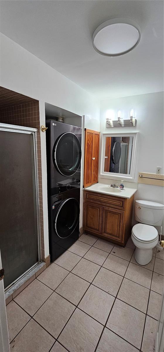 bathroom featuring stacked washer and dryer, tile patterned flooring, and a shower stall