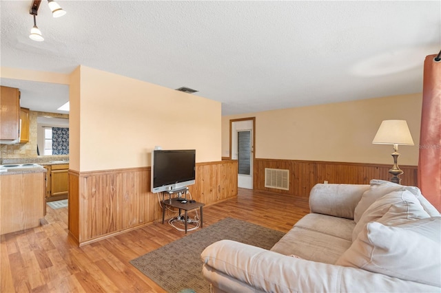 living room featuring a wainscoted wall, light wood-style flooring, a textured ceiling, and visible vents