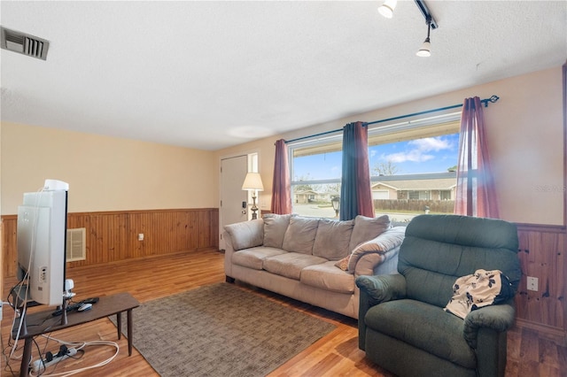 living area featuring visible vents, wainscoting, wooden walls, a textured ceiling, and wood finished floors