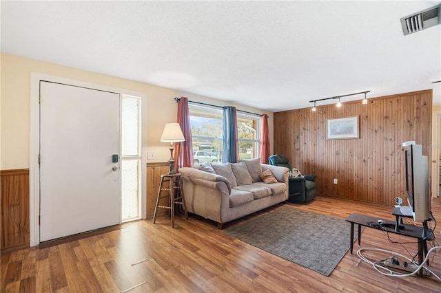 living area featuring wooden walls, visible vents, wainscoting, light wood-type flooring, and track lighting