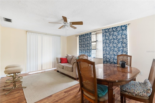 dining space featuring a ceiling fan, a textured ceiling, visible vents, and wood finished floors