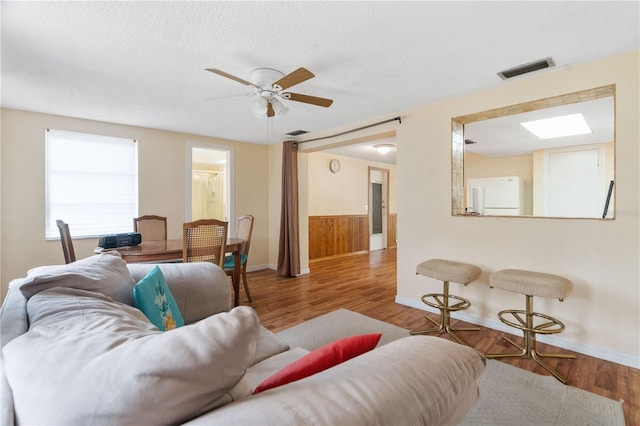 living room with a skylight, visible vents, a ceiling fan, a textured ceiling, and wood finished floors