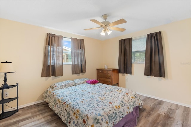 bedroom with multiple windows, ceiling fan, baseboards, and wood finished floors