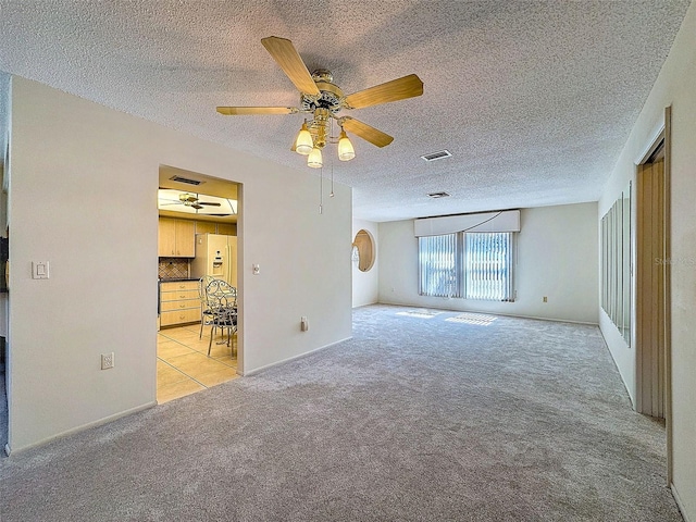 empty room with a textured ceiling, ceiling fan, visible vents, and light colored carpet