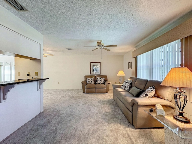 living area with ceiling fan, a textured ceiling, carpet, and visible vents