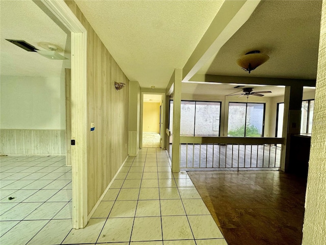 hallway with a wainscoted wall, wood walls, a textured ceiling, and light tile patterned flooring