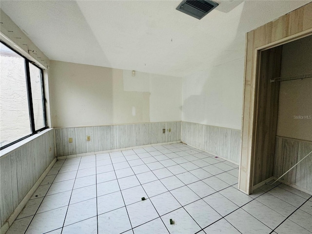 unfurnished room with wainscoting, visible vents, and wooden walls