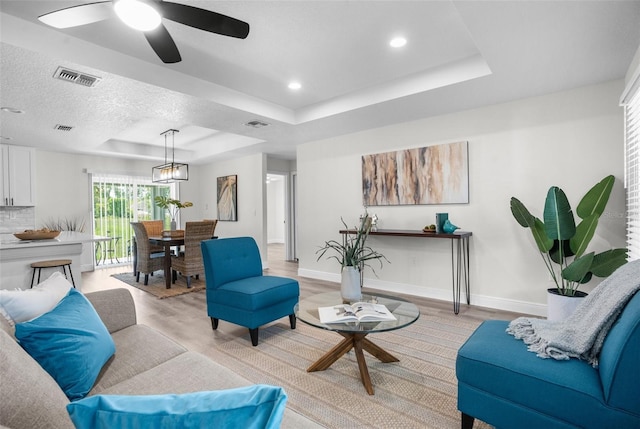 living area featuring baseboards, visible vents, a raised ceiling, light wood-style flooring, and recessed lighting