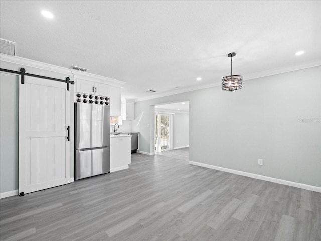 unfurnished living room featuring light wood-type flooring, a barn door, visible vents, and ornamental molding