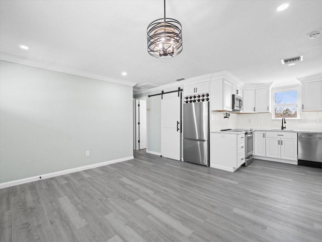 kitchen featuring stainless steel appliances, visible vents, a barn door, ornamental molding, and a sink