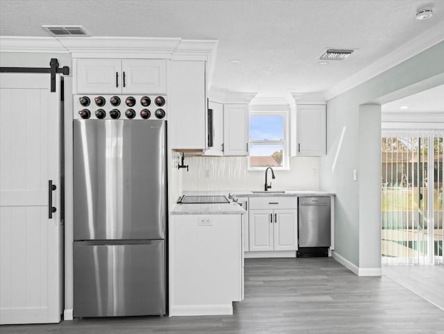 kitchen featuring appliances with stainless steel finishes, white cabinets, visible vents, and a barn door