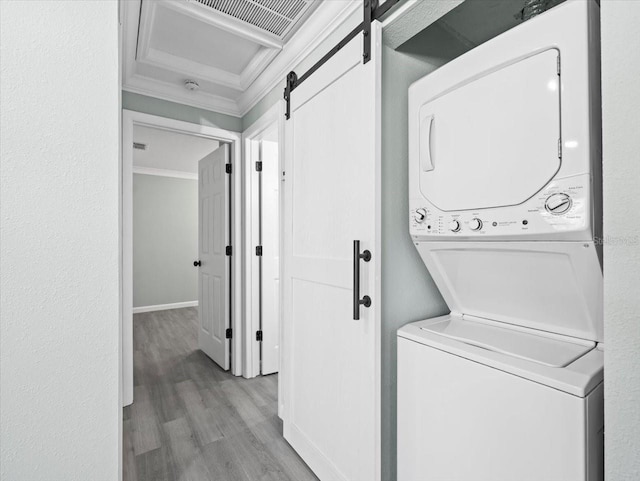 laundry room featuring laundry area, a barn door, light wood finished floors, stacked washer and clothes dryer, and crown molding