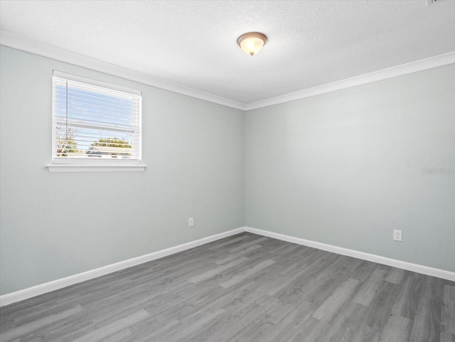 spare room with crown molding, wood finished floors, and baseboards