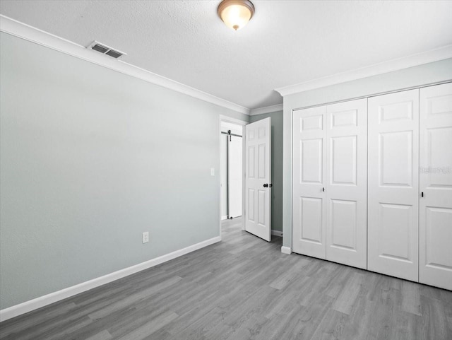 unfurnished bedroom with a barn door, wood finished floors, visible vents, baseboards, and crown molding