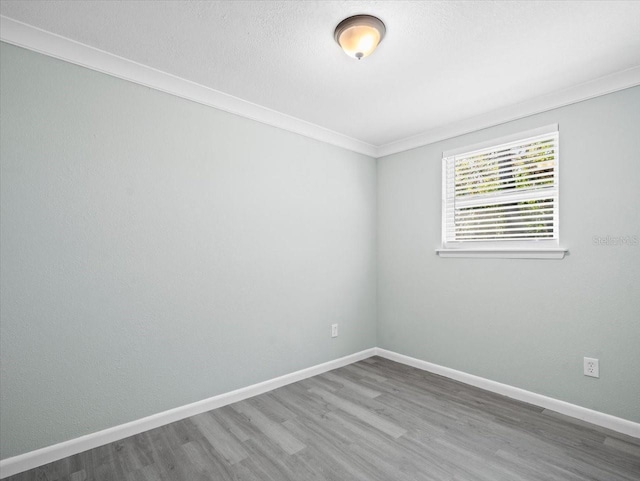 spare room featuring crown molding, a textured ceiling, baseboards, and wood finished floors