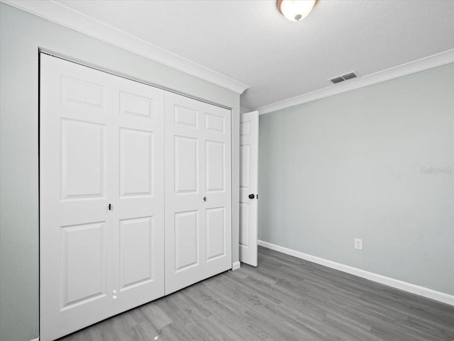 unfurnished bedroom with baseboards, visible vents, wood finished floors, crown molding, and a closet