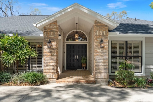 view of exterior entry with a garage, brick siding, and roof with shingles