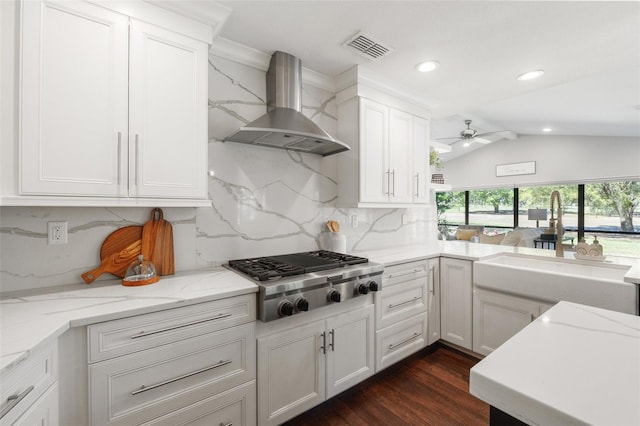 kitchen with visible vents, a sink, stainless steel gas stovetop, wall chimney range hood, and lofted ceiling