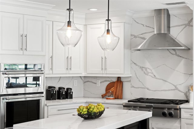 kitchen with decorative light fixtures, stainless steel double oven, white cabinets, and wall chimney exhaust hood