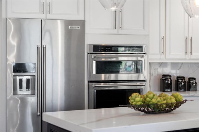 kitchen with light stone countertops, backsplash, appliances with stainless steel finishes, and white cabinetry