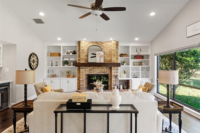 living area featuring lofted ceiling, a brick fireplace, built in features, and wood finished floors