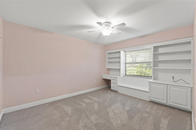 spare room featuring light carpet, built in study area, baseboards, and a ceiling fan