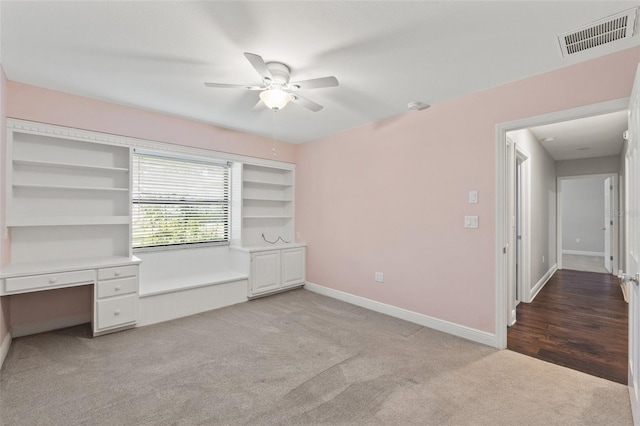 unfurnished bedroom featuring light carpet, visible vents, baseboards, and built in desk