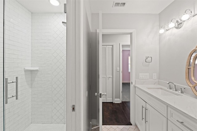 bathroom with vanity, baseboards, visible vents, and tiled shower