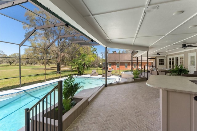 outdoor pool with a patio area, glass enclosure, a yard, and ceiling fan