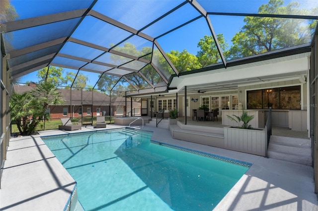 outdoor pool featuring glass enclosure, a ceiling fan, and a patio area