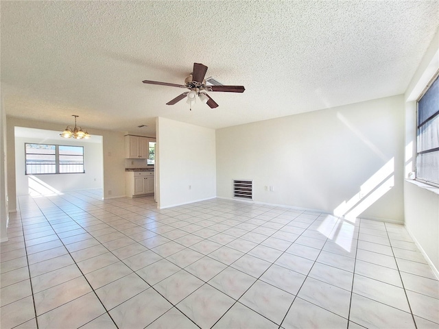 unfurnished living room with visible vents, ceiling fan with notable chandelier, a wealth of natural light, and light tile patterned flooring