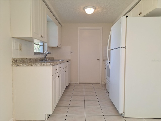 kitchen with white appliances, light tile patterned floors, a sink, white cabinetry, and backsplash