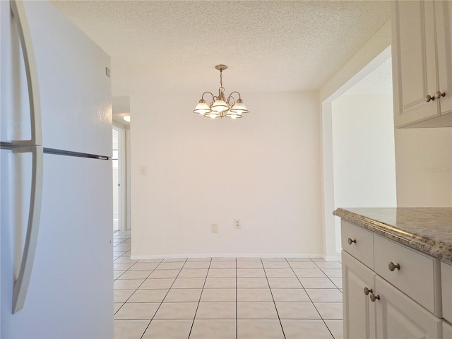 unfurnished dining area with a textured ceiling, light tile patterned floors, baseboards, and an inviting chandelier