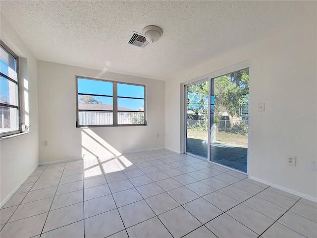 empty room with visible vents, a textured ceiling, baseboards, and light tile patterned floors