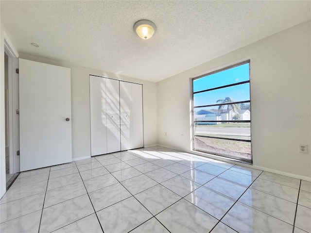 unfurnished bedroom featuring a closet, a textured ceiling, baseboards, and light tile patterned floors