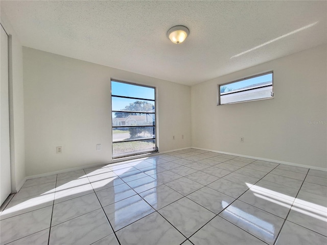 unfurnished room featuring light tile patterned floors, a textured ceiling, and baseboards