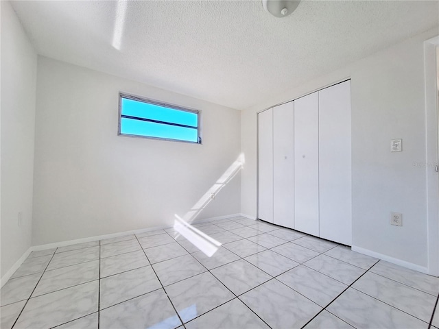 unfurnished bedroom with light tile patterned floors, a textured ceiling, baseboards, and a closet