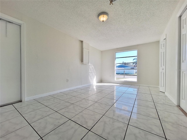 empty room featuring baseboards, a textured ceiling, and light tile patterned flooring